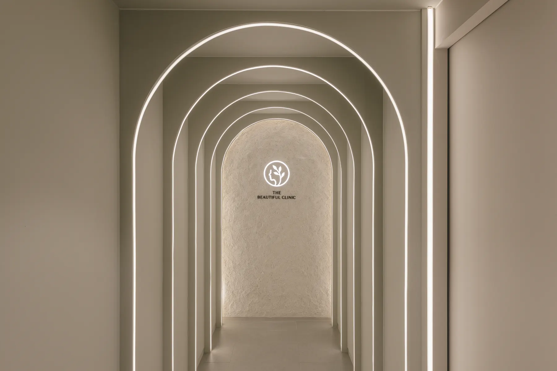 Receding arches outlined in light, leading to THE Beautiful Clinic logo on a textured wall