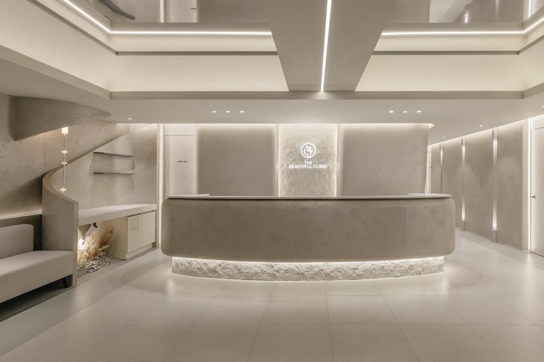Curved reception desk under the lit clinic logo at THE Beautiful Clinic in Nonhyeon, Seoul