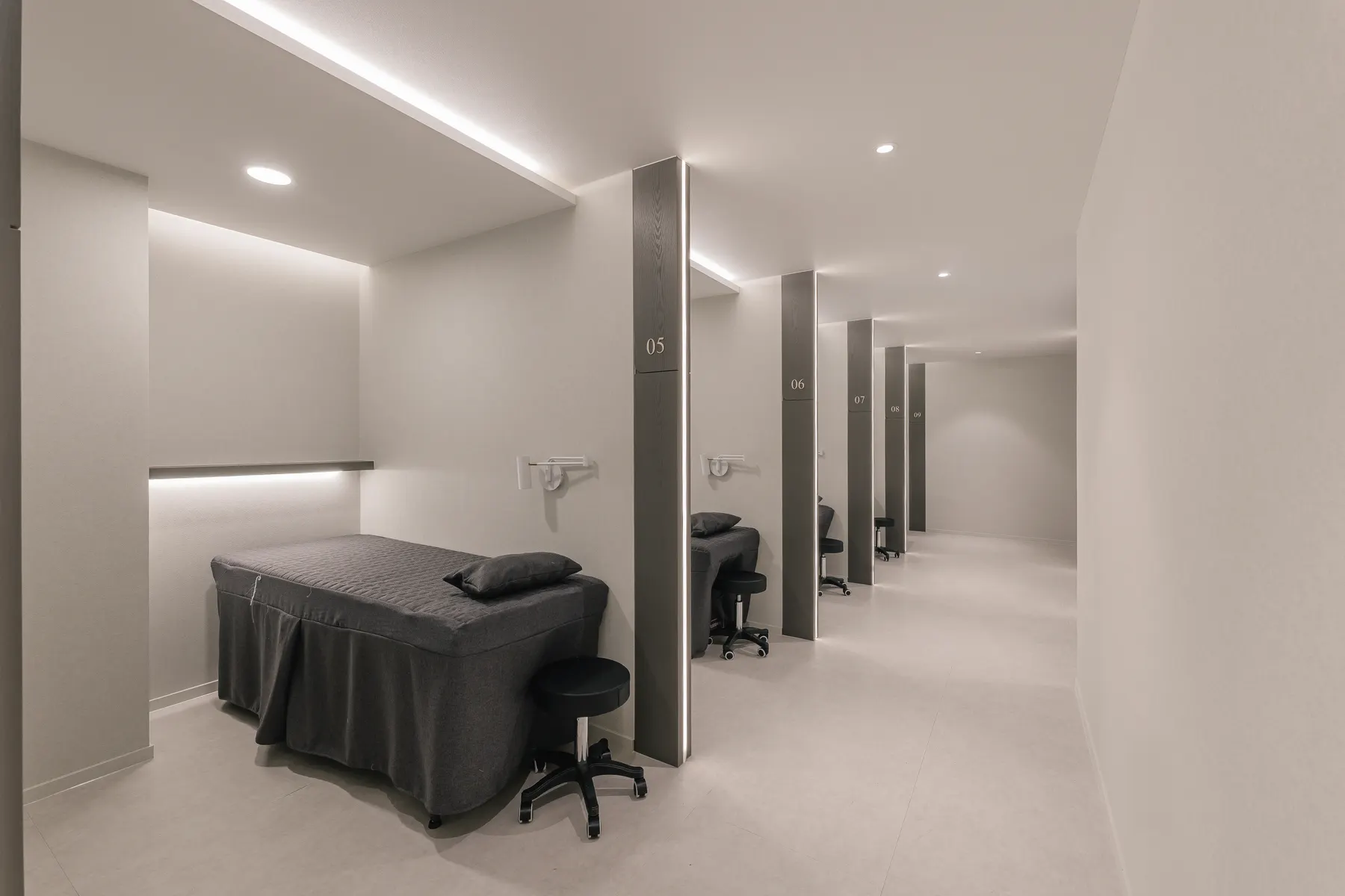 Row of numbered treatment bays with grey-covered beds and black stools under recessed lighting